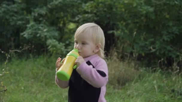 Kleines Kind trinkt aus Flasche und schaut in den Park. langsam — Stockvideo