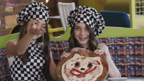 Twee jonge meisje met glimlach bekwaamheid van een pizza voor de camera — Stockvideo