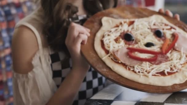 Het jonge meisje toont een pizza met een glimlach op de camera. Langzaam — Stockvideo