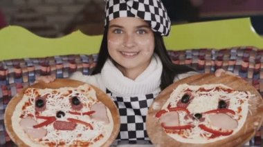 Genç kız iki pizza kameraya gösterir. Yavaş yavaş