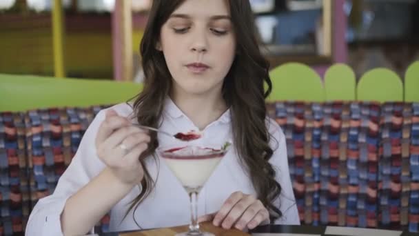 Mooie jonge meisje met glimlach eten smakelijk dessert in café. 4k — Stockvideo