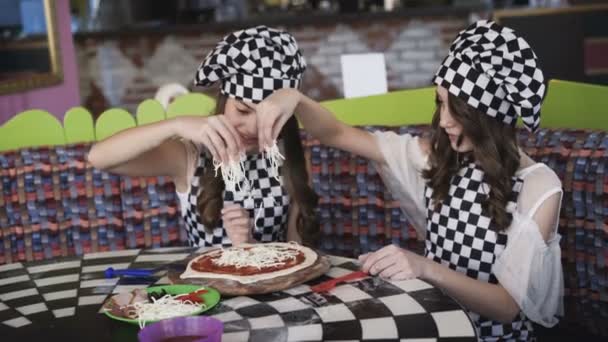 Dos muchachas alegres en uniforme que cuecen la pizza en la clase maestra en la cafetería 4K — Vídeo de stock