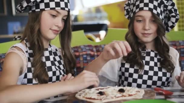 Duas meninas alegres em uniforme cozinhar uma pizza em master class no café 4K — Vídeo de Stock