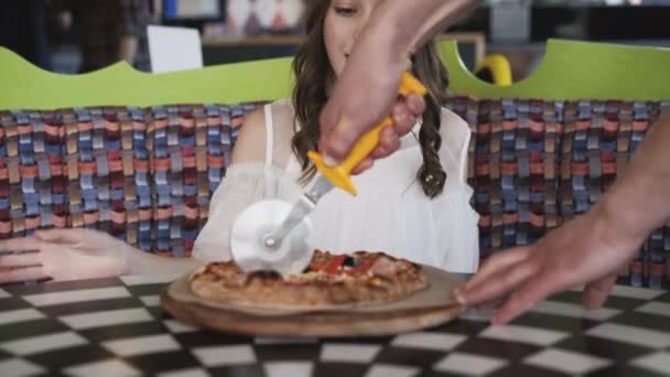 Söt flicka tittar hur kyparen skivning en pizza för henne i café. 4k — Stockvideo