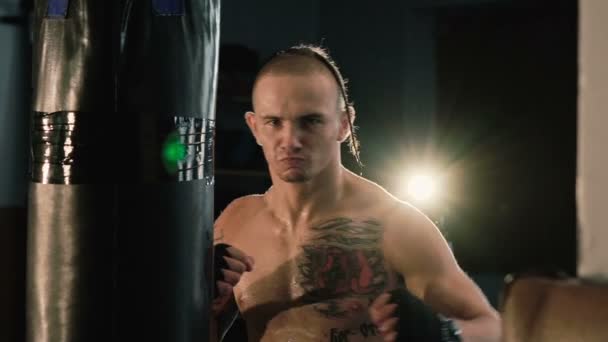 Haarloze met draadantenne op een hoofd en tatoeages, gratis vechter opleiding bokszak. — Stockvideo