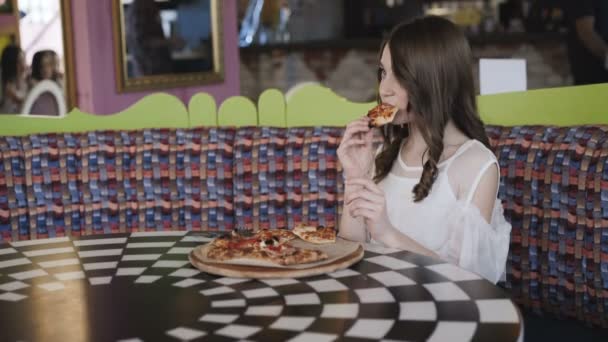 Hezká mladá dívka jíst pizzu v kavárně. 4k — Stock video