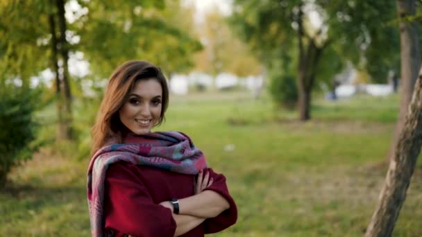 Портрет уверенной девушки в стильном шарфе, скрещивающем руки перед камерой в парке — стоковое видео