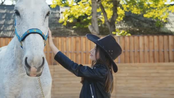 笑顔とアリーナの白い美しい馬をなでる帽子でかわいい女の子の肖像画 — ストック動画