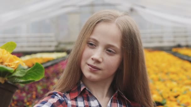 Красивая молодая девушка смотрит на цветочный горшок с улыбкой в теплице — стоковое видео