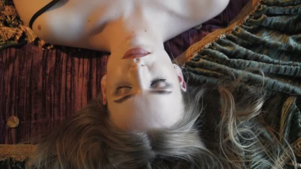 Chica bastante apasionada acostada en la cama, acaricia su cuello y mira a la cámara — Vídeos de Stock