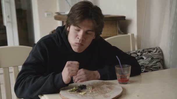 Hladová mladý muž nenasytně jíst pizzu v kavárně — Stock video