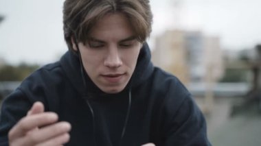 Üzgün adam akıllı telefon ve kulaklık bir sokak çatı kullanır