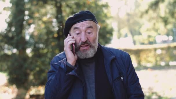 Стильный пенсионер в шляпе, эмоционально разговаривающий по телефону на солнечной улице — стоковое видео