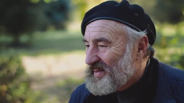 Весёлая улыбка на камеру морщинистого пожилого человека, сидит на улице — стоковое видео
