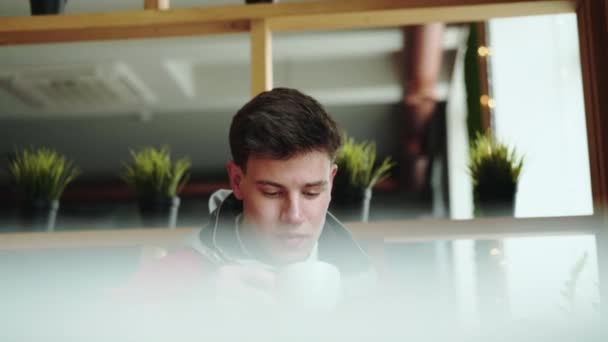 Beau jeune garçon boit une tasse de café dans un café et regarde ailleurs — Video