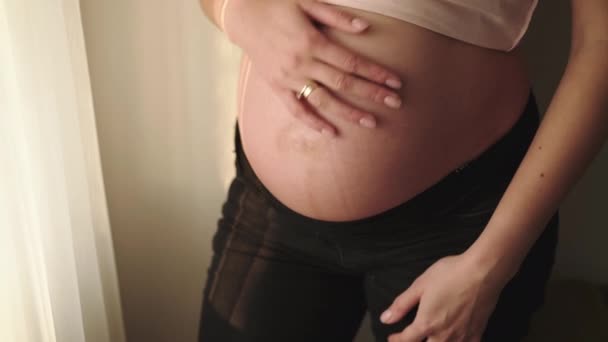 Femme enceinte méconnaissable caresse son ventre à la fenêtre dans la chambre — Video