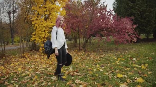 Beautiful girl walks in colourful autumn park, puts on hat and looks aside — Stock Video