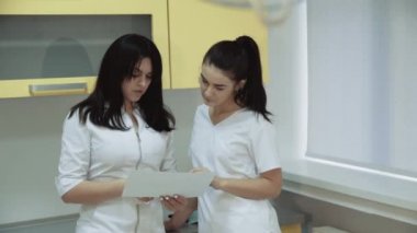 İki genç kadın diş hekimi diş hekimliği odasında danışır. 4k