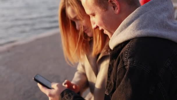 Happy man and girl using smartphone on a quay on sunset — Stock Video