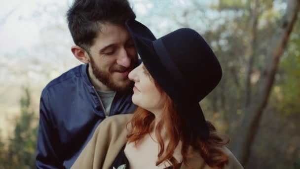 Sonriente pareja se para en abrazos, el hombre besa a su chica en el soleado parque — Vídeo de stock