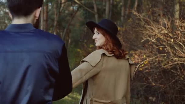 Stylish lady in hat leads her boyfriend in picturesque park — Stock Video