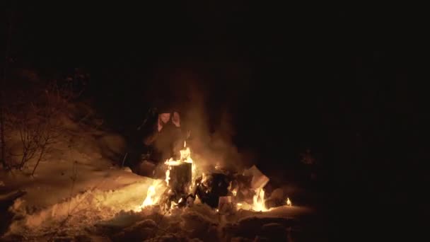 Мужчина греется у костра горящей бумагой в ночном лесу. 4K — стоковое видео