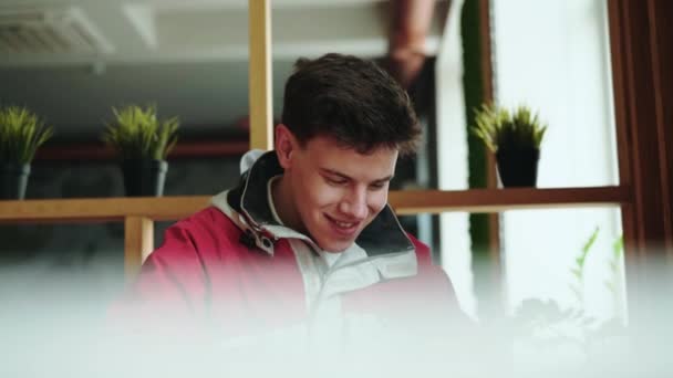 Счастливый мальчик с гаджетом в кафе, улыбается и смотрит в сторону — стоковое видео