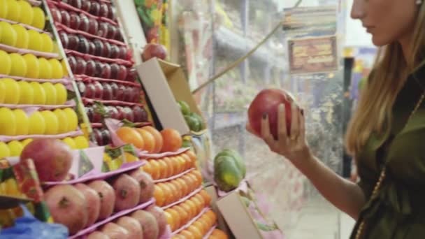 Mujer joven elige granate en la tienda de frutas. 4K — Vídeo de stock