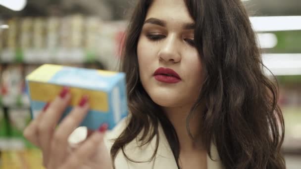 Menina sorridente lê a composição do produto em embalagens em supermercado — Vídeo de Stock
