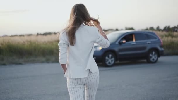 Dame en costume blanc marchant vers la voiture et posant à la caméra hors de la ville — Video