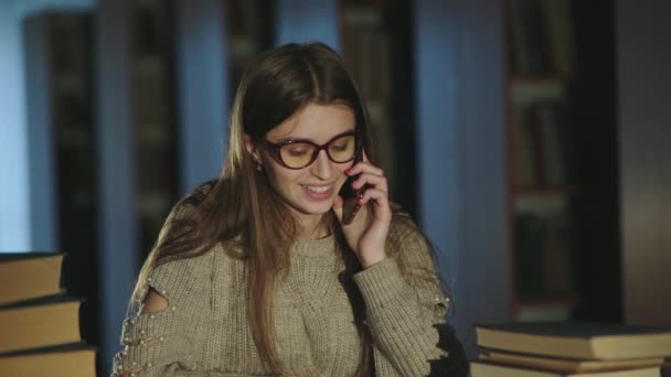 Glücklicher Student, der beim Lernen in der Bibliothek mit dem Handy spricht — Stockvideo