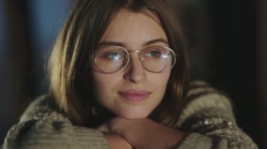 Gözlüklü, kitaplara yaslanmış, kameraya gülümseyen uzaktaki bir öğrencinin portresi.