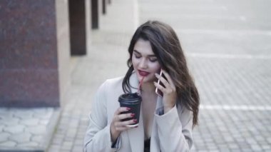 Mutlu kız telefonda konuşuyor, gülümsüyor ve sokakta içiyor.