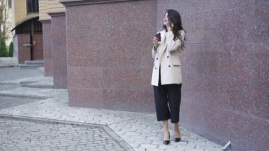 Şık giyinmiş, telefonda konuşan ve kahve içen oyuncu bir kız.