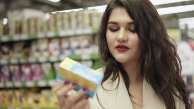 Mutlu kadın süpermarkette ambalajın bileşimini okuyor.