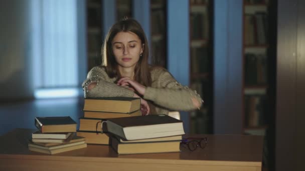 Retrato de una hermosa chica apoyada en libros y sonriendo a la cámara en la biblioteca — Vídeos de Stock