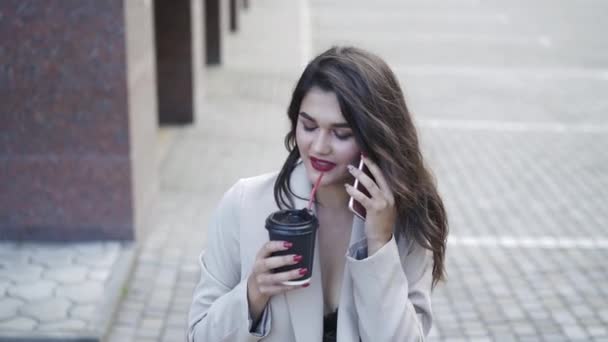 Chica feliz habla por teléfono con una sonrisa y bebidas en la calle — Vídeo de stock