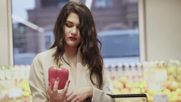 Mooie vrouw onderzoekt een rode peper in een supermarkt en zet het in een mand — Stockvideo