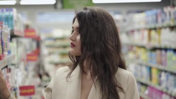 Portrait de jolie femme réfléchie examine les marchandises sur les étagères des supermarchés — Video