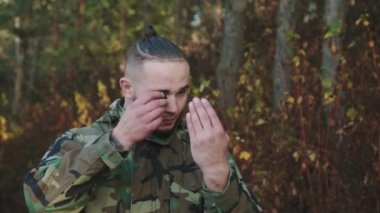 Kamuflajlı asker ormanda yüzüne is bulaştırıyor.