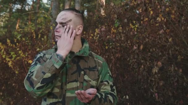 Il soldato coraggioso in camuffamento spalma strisce di fuliggine su faccia a una foresta prima di lotta — Video Stock