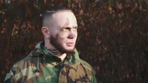 Soldat en camouflage et bandes de suie sur le visage regardant la lumière du soleil et à la caméra — Video