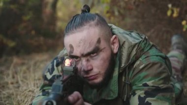 Asker portresi orman yolunda yatıyor ve tüfekle kameraya nişan alıyor.