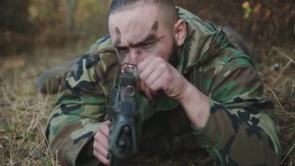 Retrato de soldado con tiras de hollín en la cara se encuentra en un camino y apunta con rifle — Vídeos de Stock