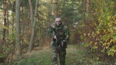 Asker ormanda tüfekle koşuyor ve operasyon sırasında etrafa bakıyor.