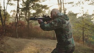 Vahşi asker, gün batımında ormanda tüfekle objeye nişan alır.