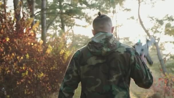 Вид ззаду солдата ходьба на захід сонця в лісі з рушницею на плечі — стокове відео
