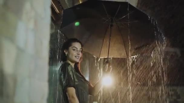 Страстная мокрая брюнетка позирует с зонтиком под ночным ливнем — стоковое видео