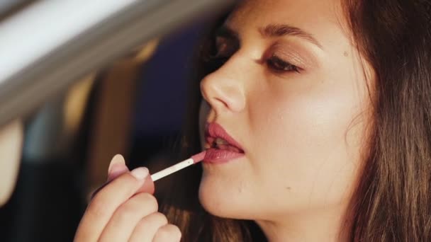 Close view of pretty long-haired girl applying lipstick at car front mirror. — Stock Video