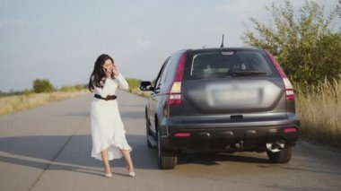 Endişeli, yalnız iş kadını şehir dışında bozuk bir arabada telefonla konuşuyor.